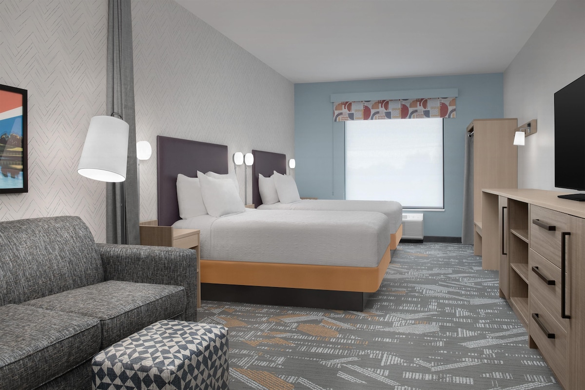 A modern hotel room with a bed, a sofa, a TV, and a desk.