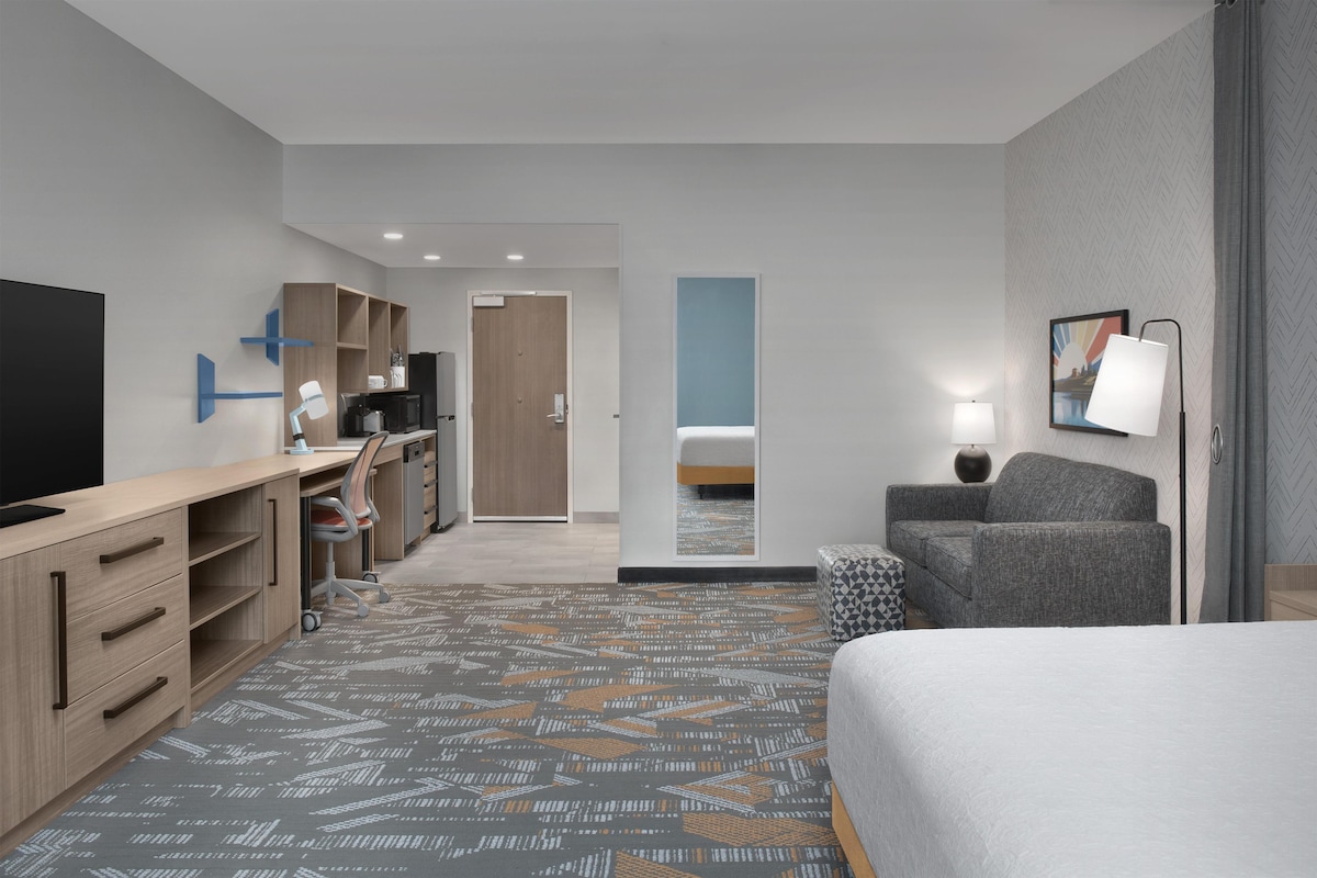 A hotel room with a bed, desk, chair, and a small sofa.