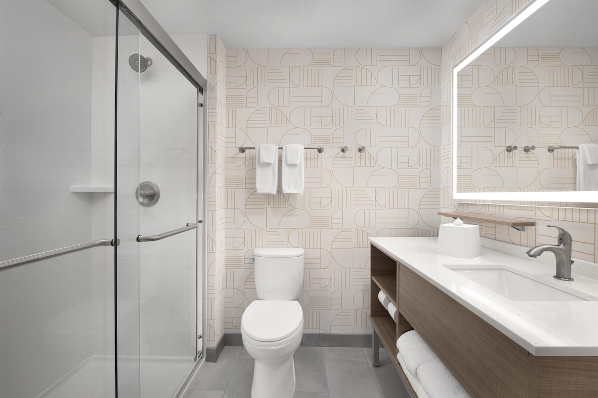 Une salle de bain moderne avec une douche à parois de verre, des toilettes blanches et un meuble-lavabo en bois doté d’un évier et d’un miroir.