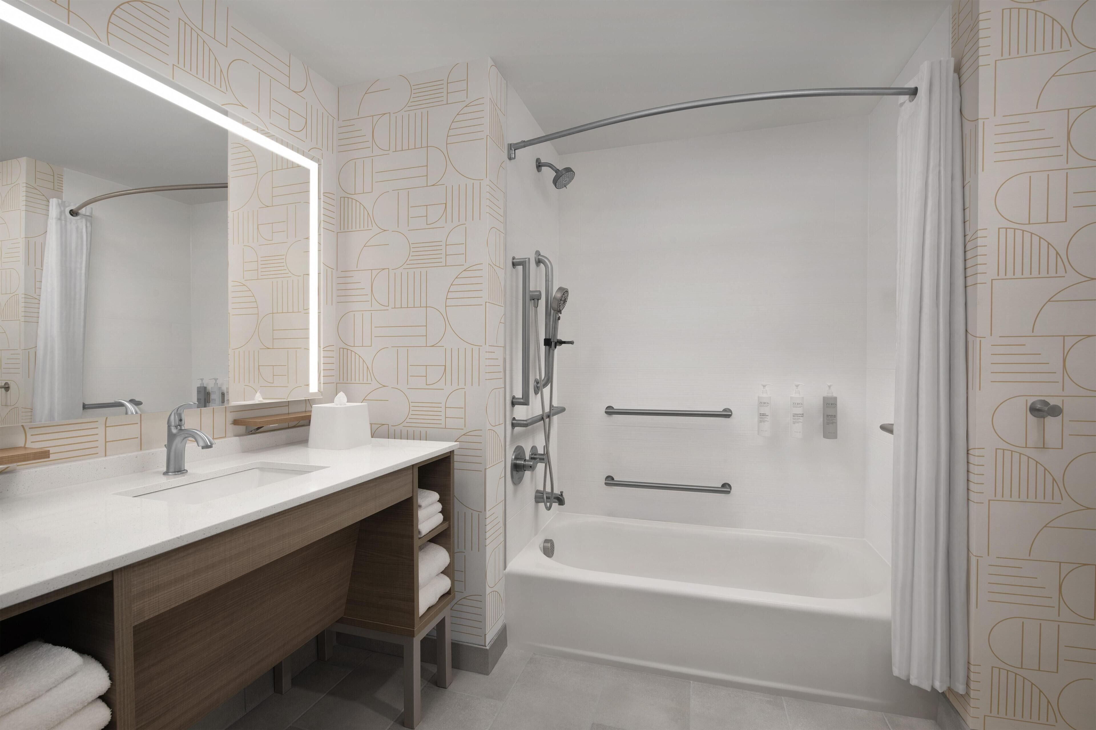 A modern bathroom with a large mirror, a sink, a bathtub, and a shower.