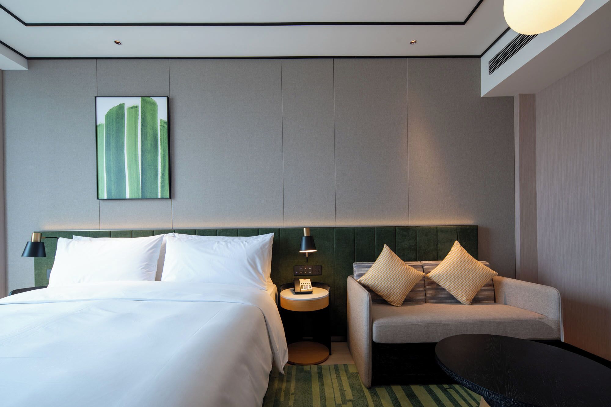 Ein Hotelzimmer mit Bett, einer Couch, einem kleinen Tisch, einer Lampe und einem Bild an der Wand.