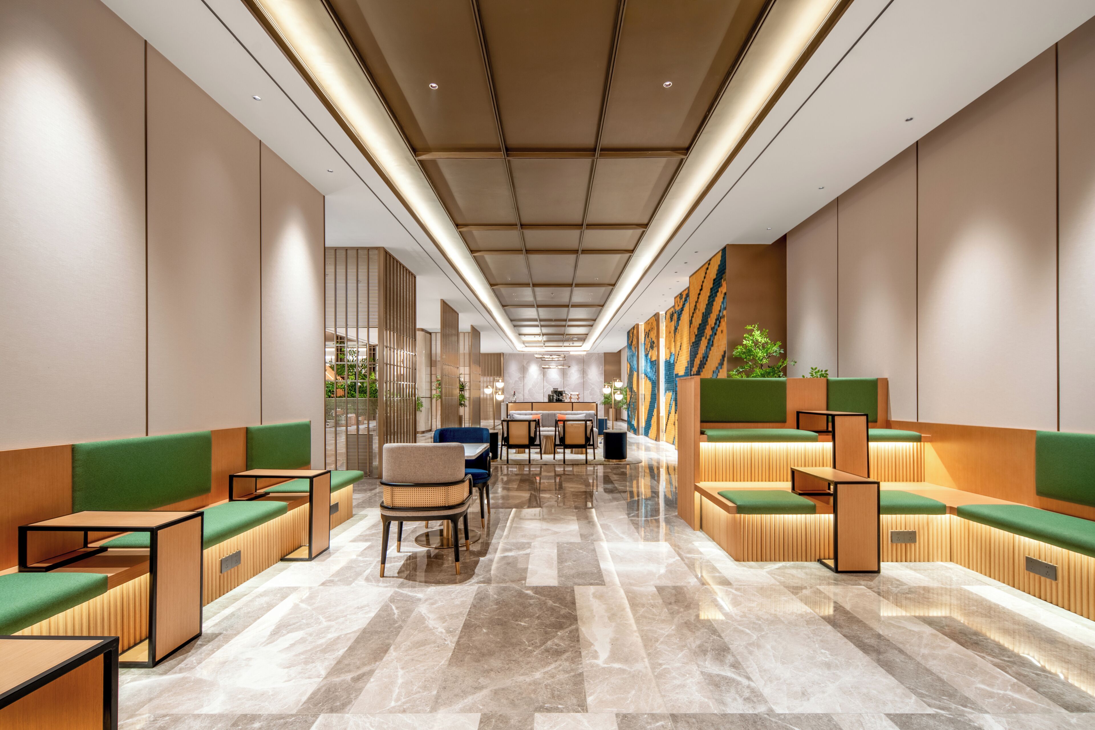 A modern hotel lobby with seating areas, a central dining table, and a kitchen in the background.