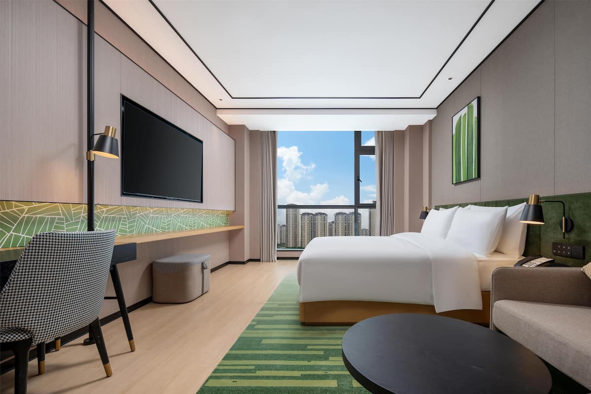 Habitación de hotel con cama, escritorio, silla, televisor y vistas a la ciudad.
