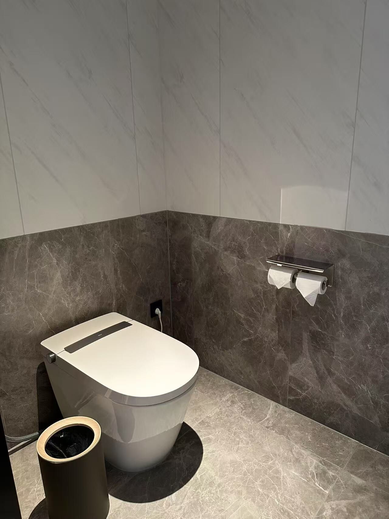 A modern bathroom with a toilet, a trash can, and a towel rack.