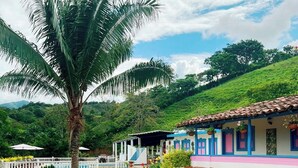 A two-story building with a tiled roof, a staircase leading to the upper floor, and a well-maintained garden with a palm tree and a fountain. - HOTEL JARDIN DEL RIO  (Betania)