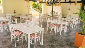 A spacious outdoor dining area with white tables and chairs, a staircase leading to an upper level, and a potted plant in the foreground. - HOTEL JARDIN DEL RIO  (Betania)