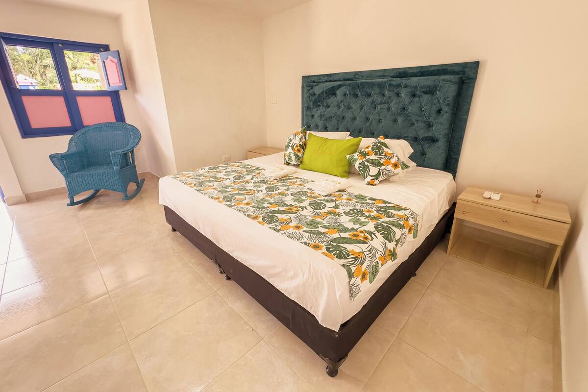 A bedroom with a bed, a nightstand, a chair, and a window with a view.