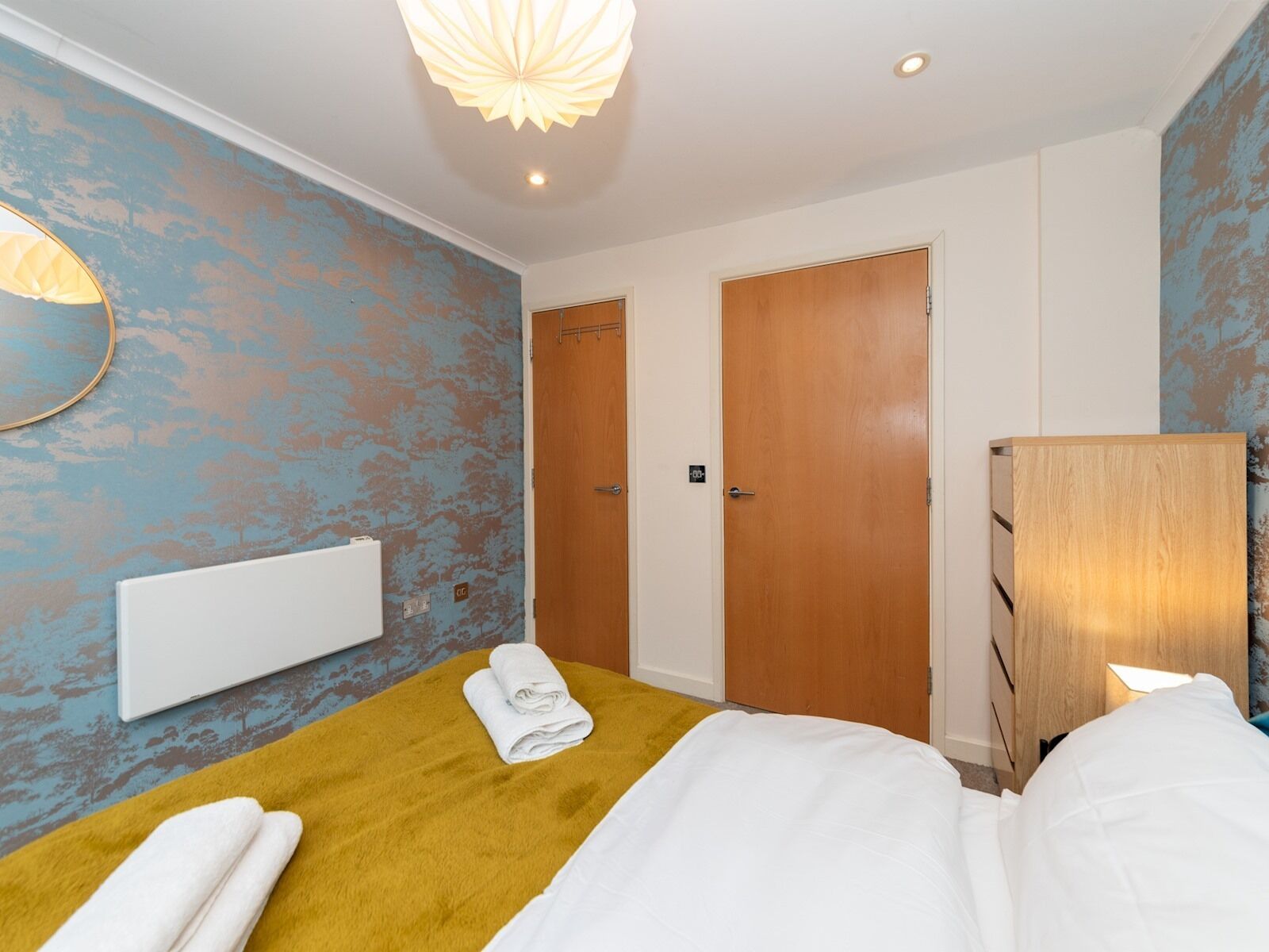 A hotel room with a bed, a wooden wardrobe, a mirror, and a wall with a distressed blue paint finish.