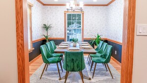 Une salle à manger avec une vue encadrée par des éléments en bois, un lustre, des chaises recouvertes d’un tissu vert et un mur à motifs de marbre.