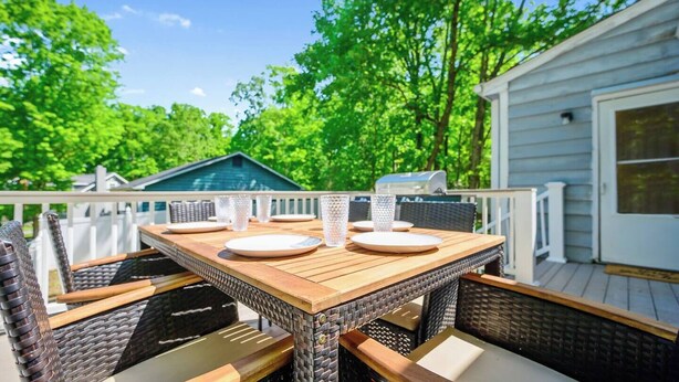 Une terrasse en bois avec une table dressée pour quatre personnes, entourée de chaises en osier.