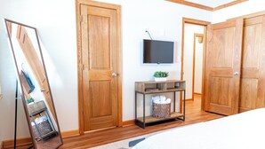 Une chambre avec des portes en bois, un téléviseur fixé au mur, une table de chevet avec une plante et un miroir appuyé contre le mur.