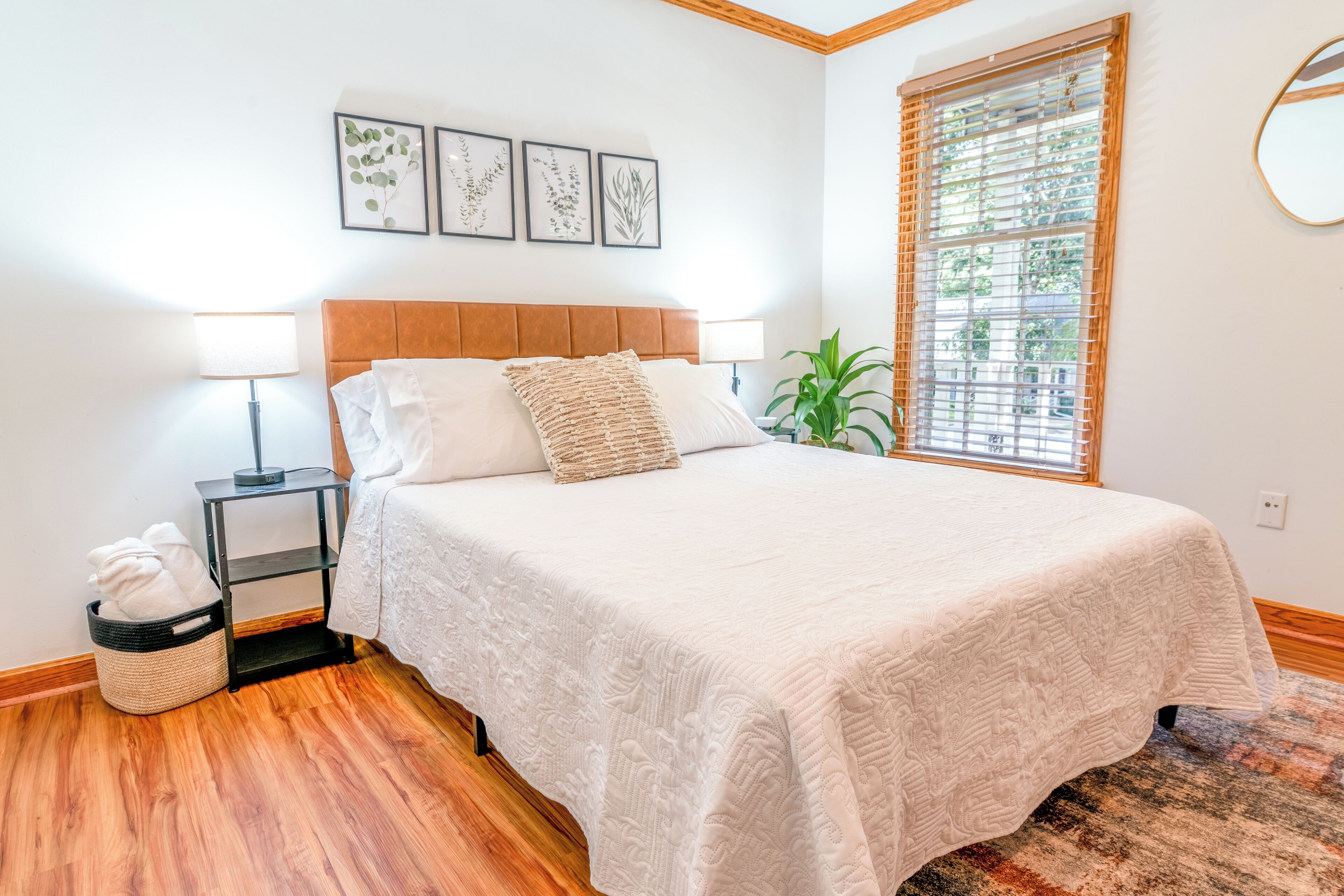 A bedroom with a bed, bedside lamps, a small plant, and framed artwork on the wall.