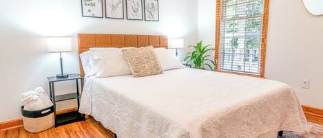 A bedroom with a bed, bedside lamps, a small plant, and framed artwork on the wall.