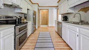 Une cuisine étroite avec des meubles blancs, des appareils électroménagers en acier inoxydable et un plancher en bois.