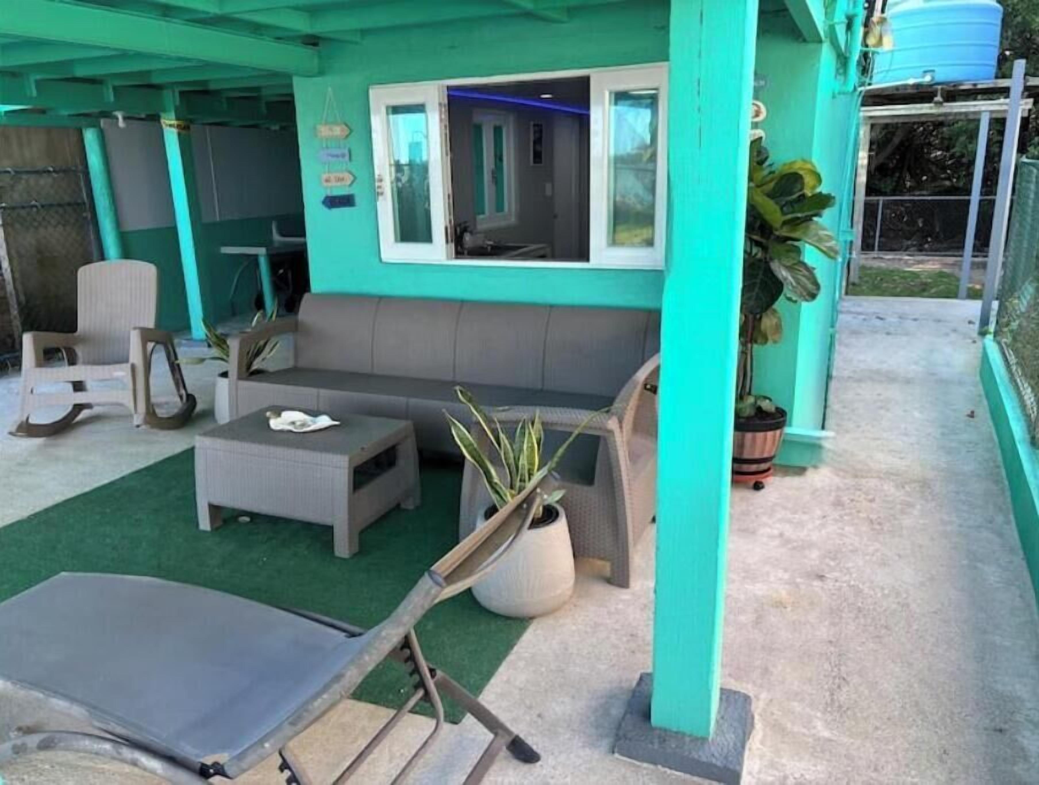Un espace extérieur aménagé avec un canapé gris, une petite table et un fauteuil. On aperçoit, à l’arrière-plan, des plantes en pot et un réservoir d’eau.