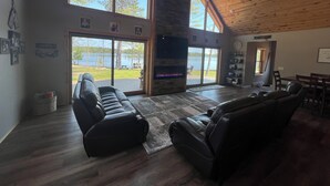 Un salon spacieux doté d’une cheminée, de grandes fenêtres et offrant une vue sur un lac.