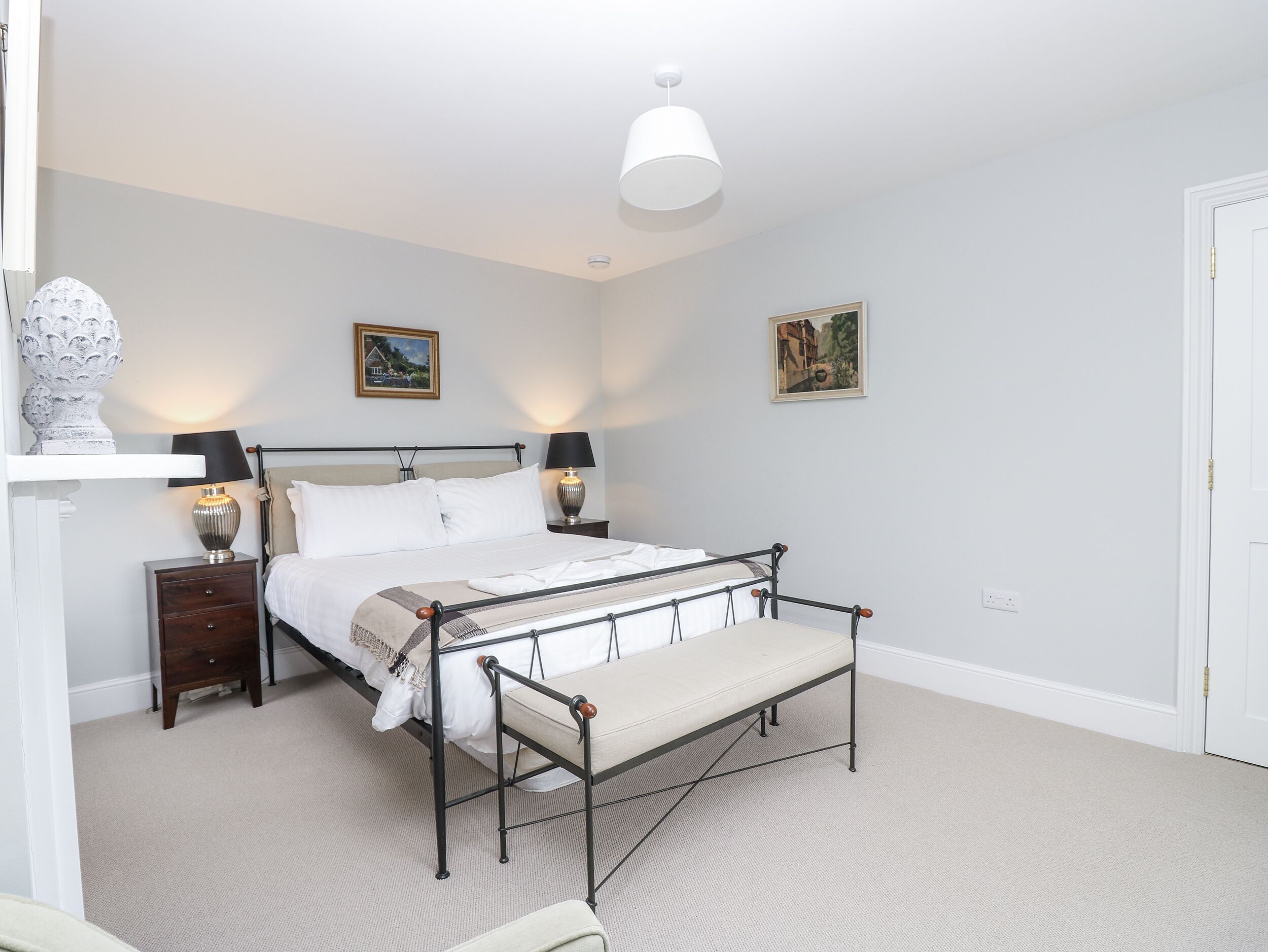 A neatly arranged bedroom with a bed, bedside tables, a bench, and two wall-mounted lamps.