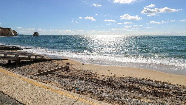 A beach with a clear sky, calm sea, and rocky outcrops. - Milston (Ventnor)