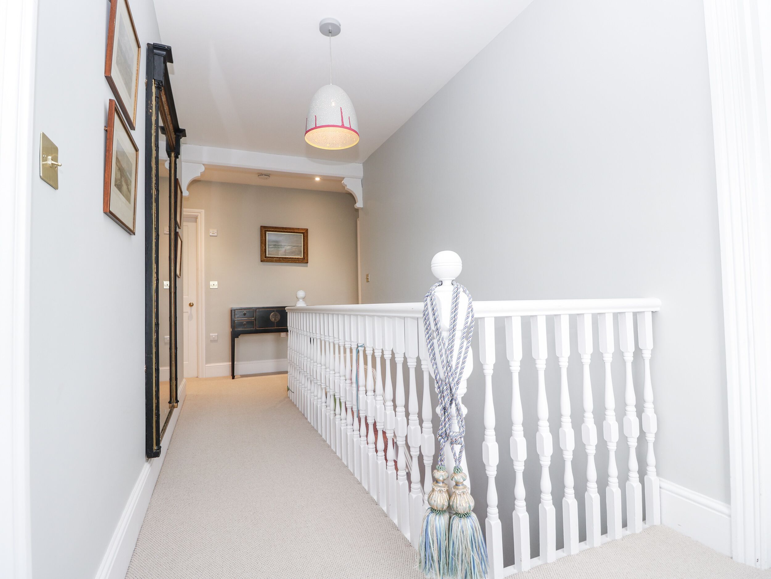 A hallway with a white railing, a hanging light fixture, and a mannequin with a scarf.
