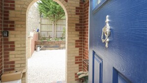 A brick archway leading to a gravel pathway, a blue door with a metal handle, and a wooden bench. - Milston (Ventnor)