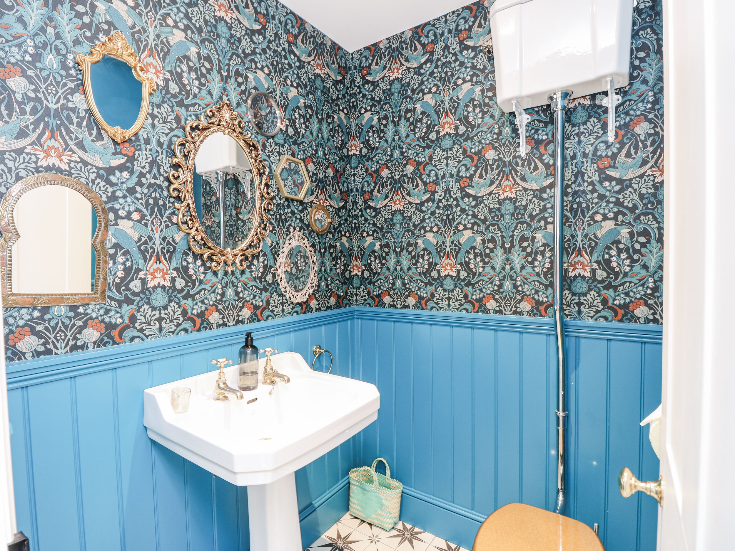 A bathroom with a blue wainscoting, a white pedestal sink, and ornate mirrors.