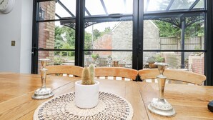 A wooden table with a woven placemat, two white ceramic planters with cacti, and a clock on the wall. - Milston (Ventnor)