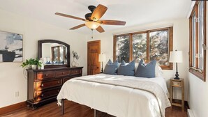Un dormitorio con cama, cómoda, ventilador de techo, ventana y mesita de noche con lámpara.