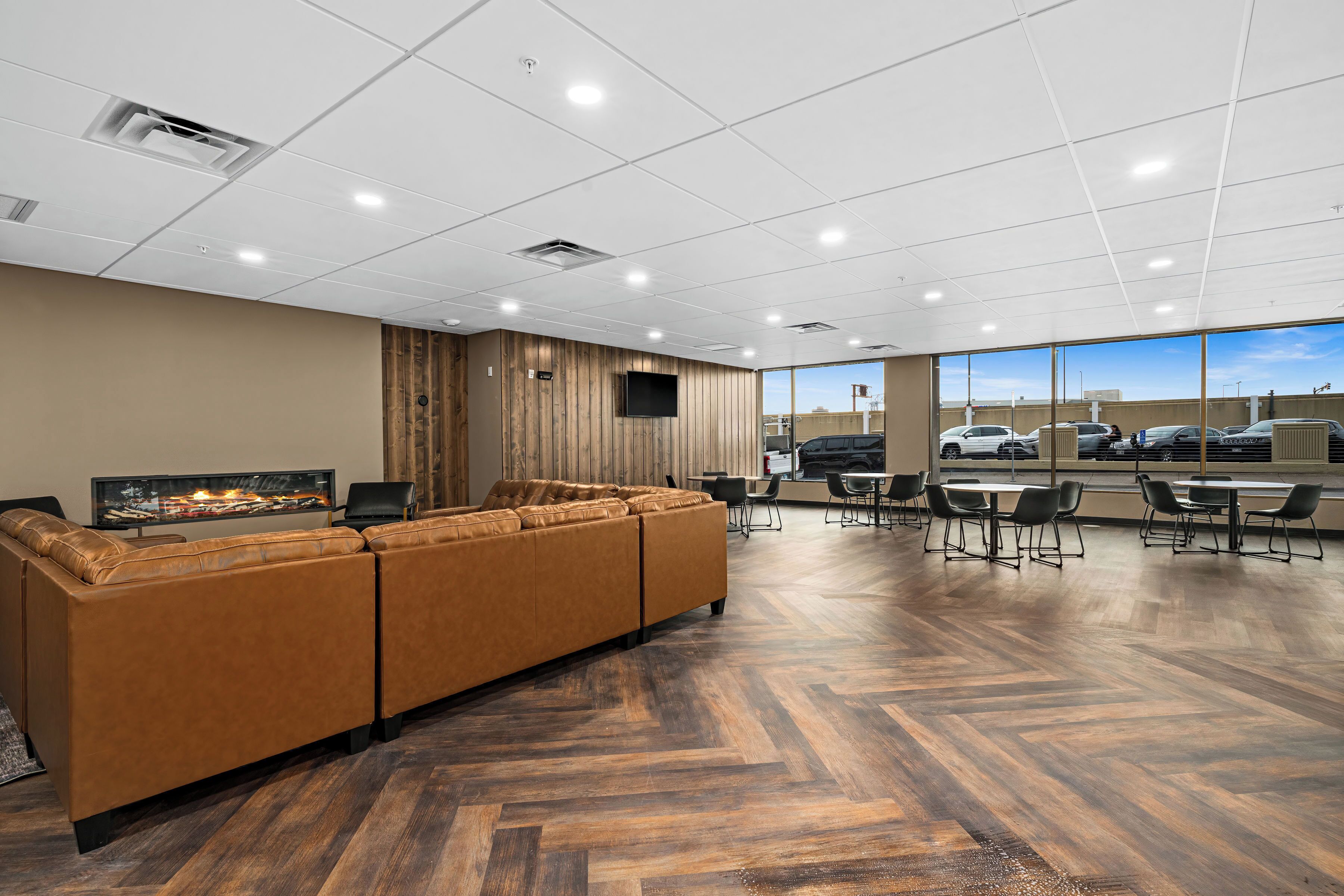 A modern lounge area with a large sectional sofa, a flat-screen TV, and a herringbone wood floor.