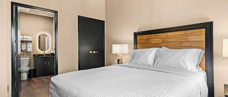 A hotel room with a large bed, a wooden headboard, a bedside lamp, and a door leading to a bathroom.