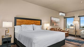 A hotel room with a large bed, a desk with a lamp, a chair, and a view of the city through the window.