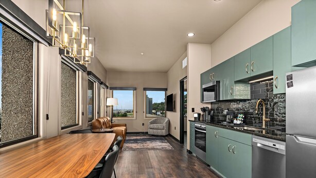 A modern kitchen with a dining area, large windows, and a view of the outdoors.