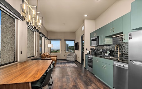 A modern kitchen with a dining area, large windows, and a view of the outdoors.