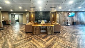 A spacious lobby with a herringbone wood floor, a central seating area with a wooden coffee table, and a television mounted on the wall.