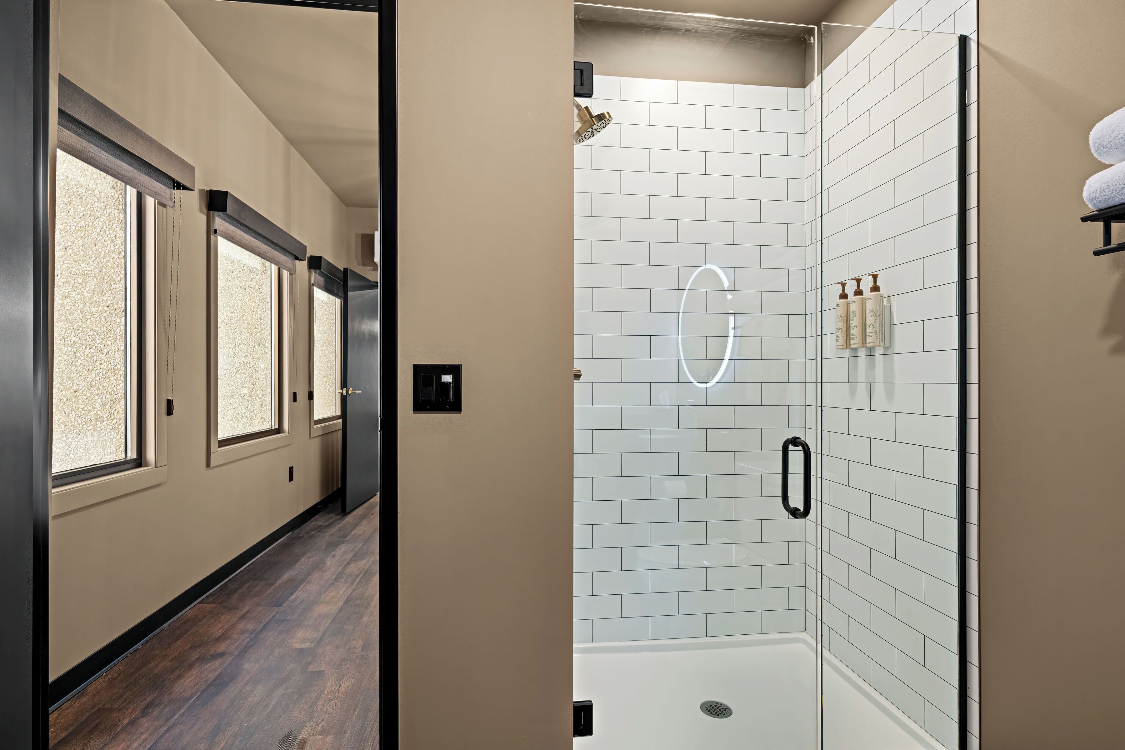 A modern bathroom with a glass shower enclosure, white tiled walls, and a wooden floor.