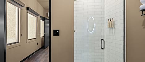 Un baño moderno con cabina de ducha de vidrio, paredes de azulejos blancos y suelo de madera.