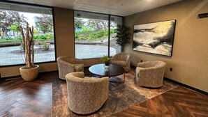 A modern interior with a round table, four upholstered chairs, a large abstract painting, and a potted plant.