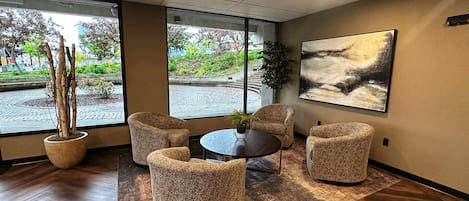 A modern interior with a round table, four upholstered chairs, a large abstract painting, and a potted plant.