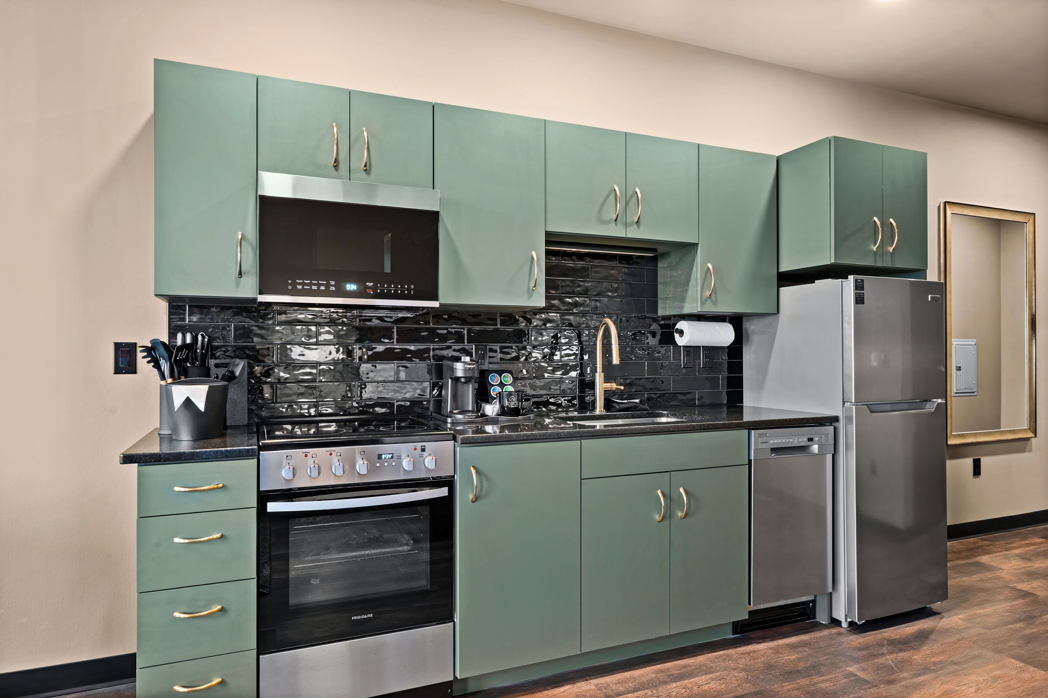 A modern kitchen with green cabinets, stainless steel appliances, and a black backsplash.