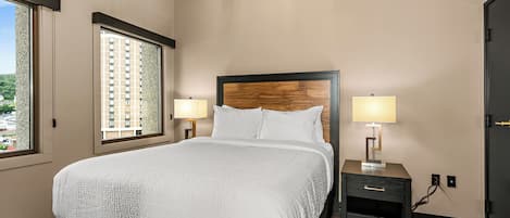 A neatly arranged hotel room with a large bed, two bedside lamps, a nightstand, and a view of a building through the window.