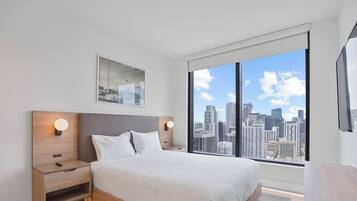 A modern hotel room with a large bed, two bedside tables, a city view, and a framed picture on the wall.