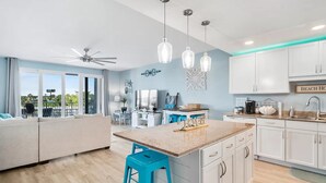 Een moderne keuken met witte kasten, een centraal eiland met krukken, hangende verlichting en een plafondventilator.