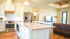 A modern kitchen with white cabinetry, a central island, stainless steel appliances, and a wooden floor. - St George Island Home with Private Pool, Pet Friendly (heated/cooled pool for a fee) (Eastpoint)