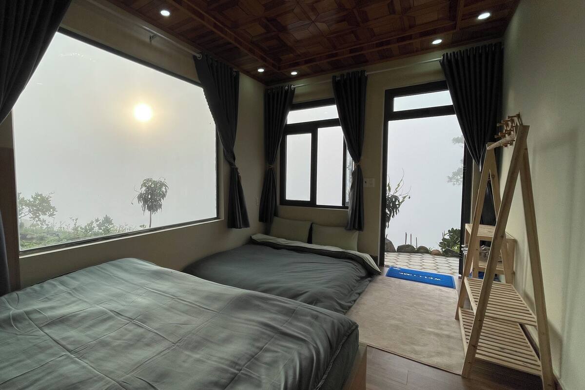 A room with two beds, large windows, and a view of the outside.