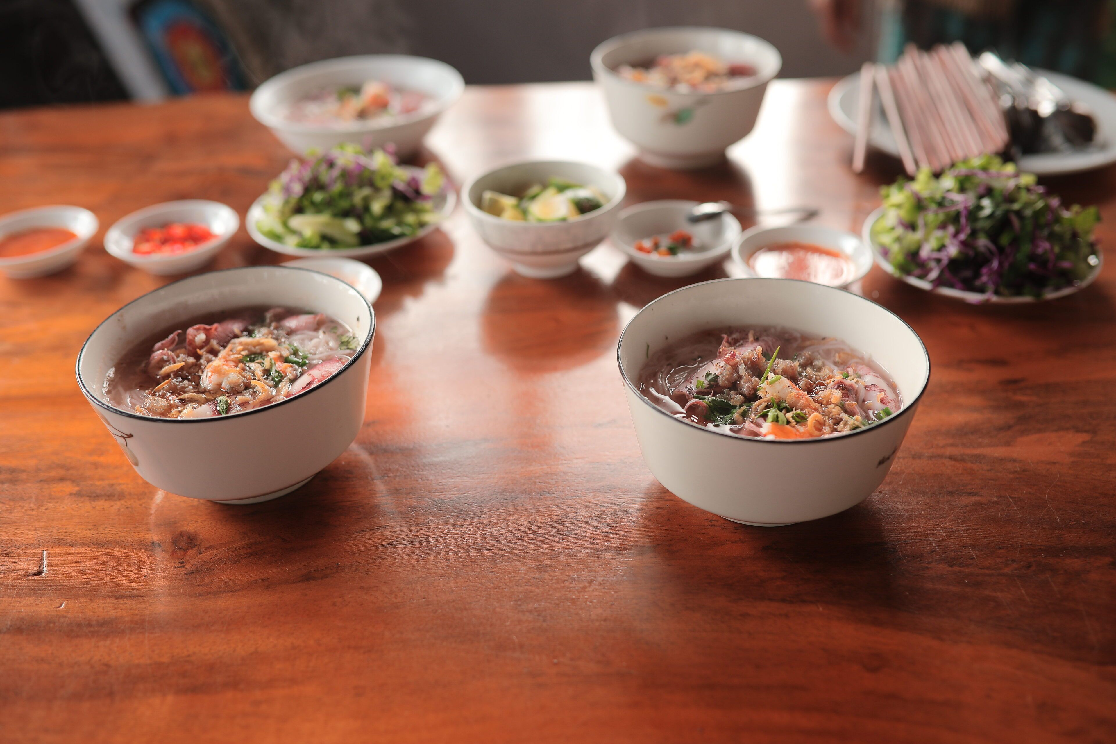 A wooden table with several bowls of soup and side dishes.
