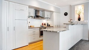 A modern kitchen with white cabinetry, a central island, and a built-in oven. - Space Style and Comfort (Auckland)