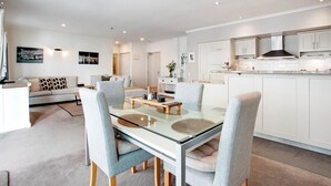 A modern kitchen with white cabinets, a glass dining table, and a built-in stove. - Space Style and Comfort (Auckland)
