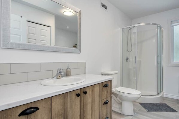Une salle de bain avec un lavabo blanc, un miroir, des toilettes et une cabine de douche en verre.