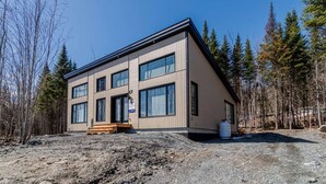 Moderni kaksikerroksinen rakennus, jossa on suuret ikkunat, puinen terassi ja sorapäällysteinen ajotie.
