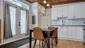 A modern kitchen with white cabinets, a dining table with chairs, and a wooden ceiling. - Hôtel à la maison - Le Cocon, ski et golf (Adstock)