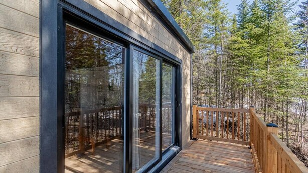 A modern building with large glass windows and a wooden deck. - Hôtel à la maison - Le Cocon, ski et golf (Adstock)